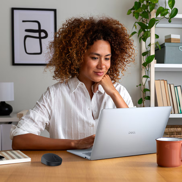 A woman sits at desk using her Dell laptop, the room is well lit.
