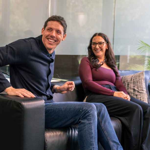Two staff sit on a sofa together laughing.