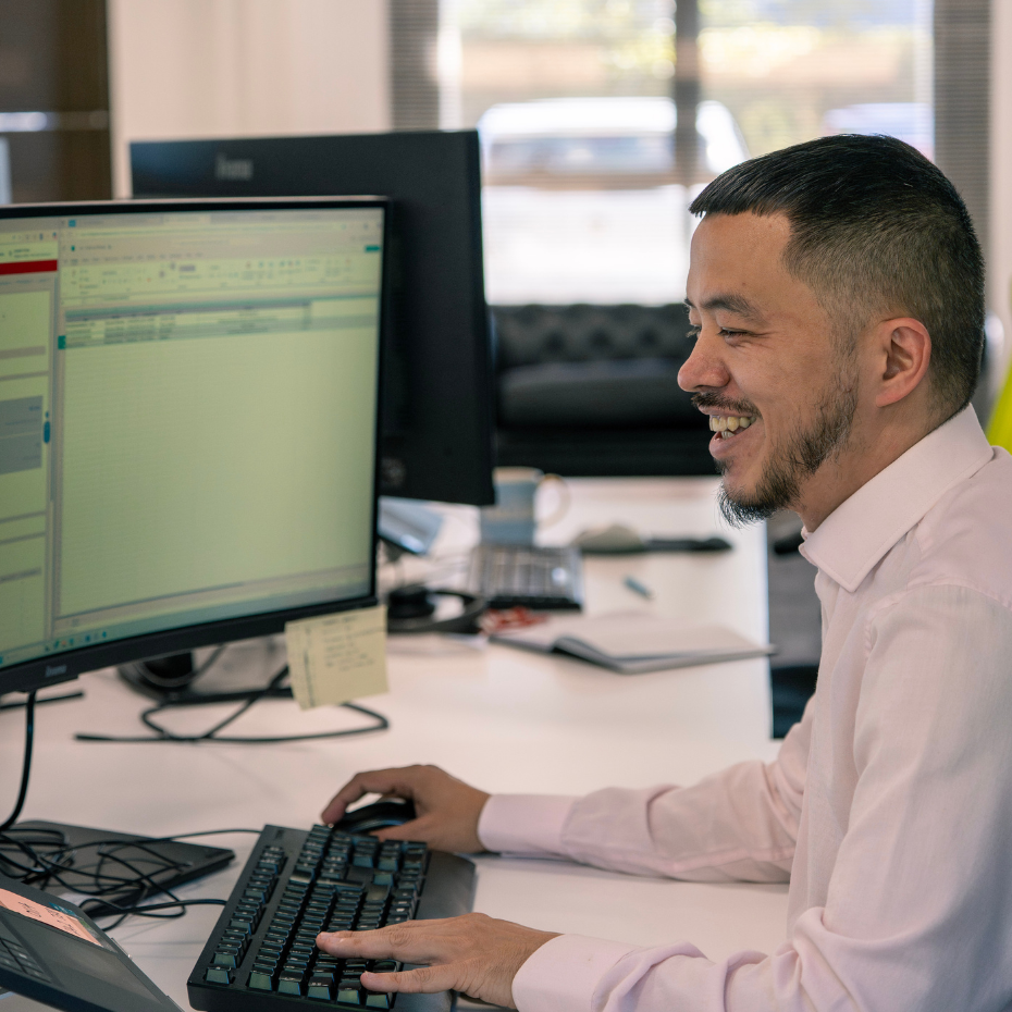A male team members is working at his desk smiling.
