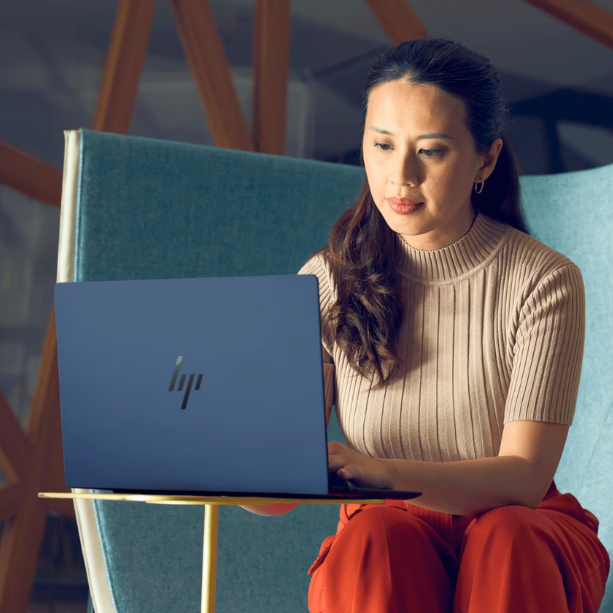 Woman sits on her HP laptop at a small table, she's working on it.