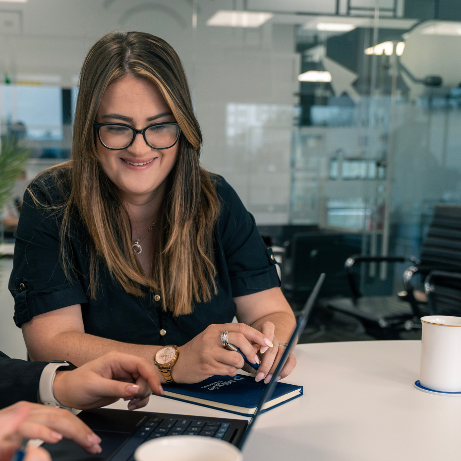 A female team member smiles as she looks at a laptop in a meeting room.