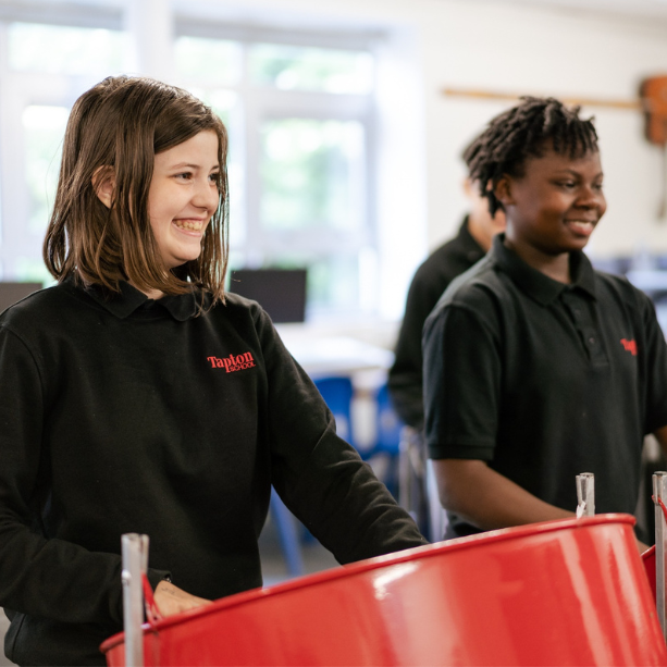 Two students smiling and using steel drums.