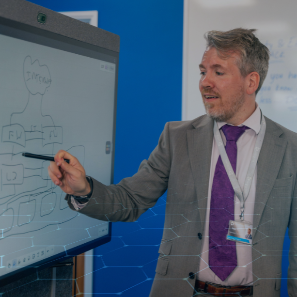 A Millgate team member dressed in a suit stands in front of a board displaying cyber security information. 