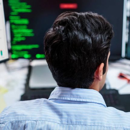 Close up of the back of a worker's head as he looks at his desktop screen.