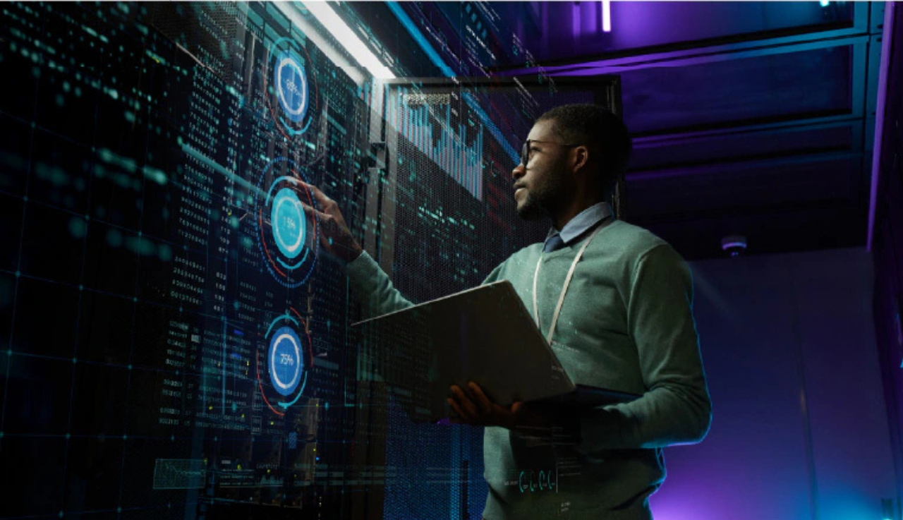 Man holds a laptop and works on a server in a dark room.