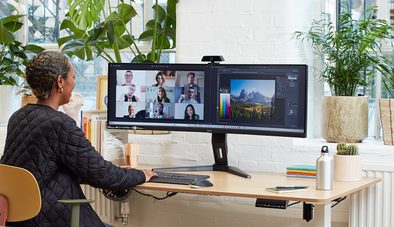 A woman sits at her desk and she is facing her monitors whilst on a video call.