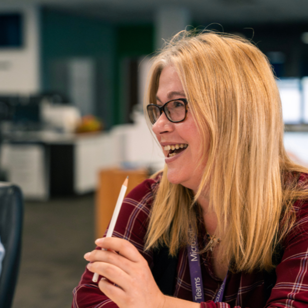 Close up of female team member laughing, she holds a pencil.
