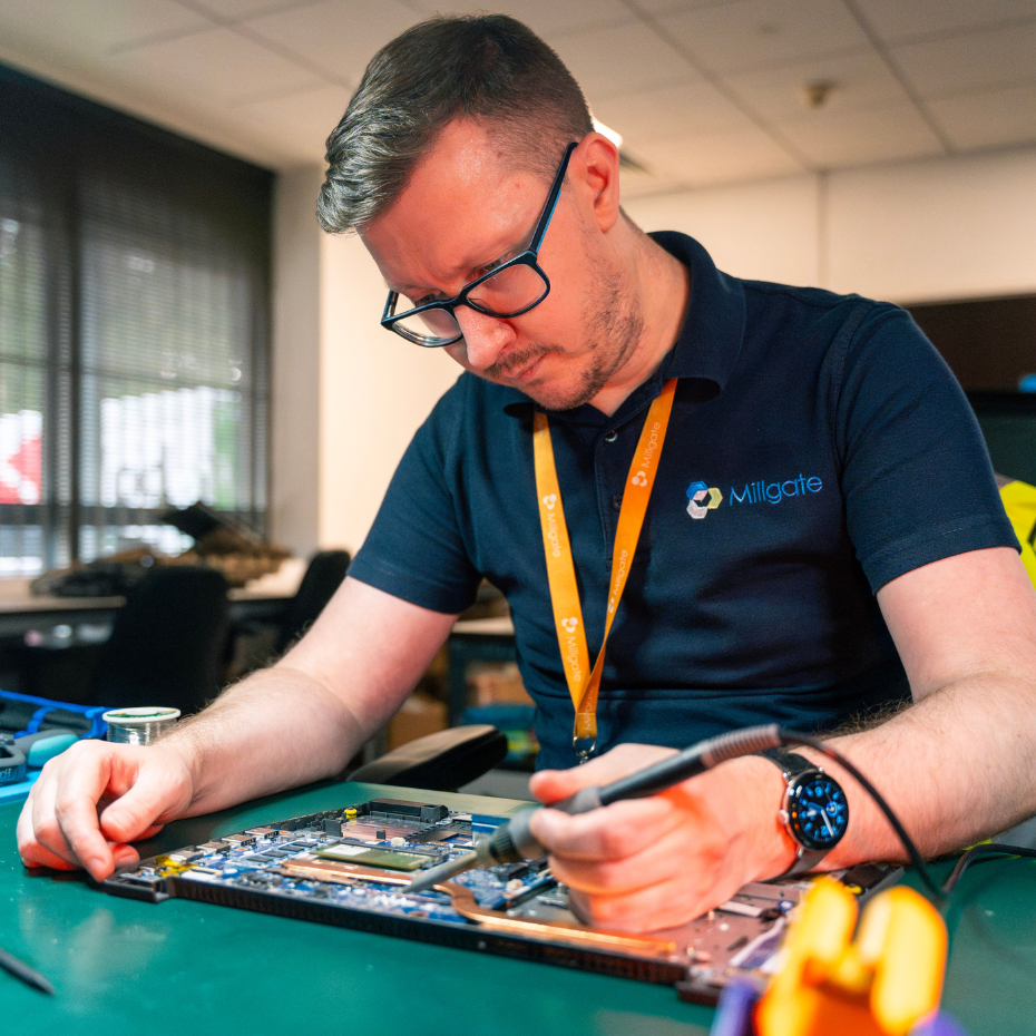 A tech expert sits at a desk as he works on soldering a motherboard.