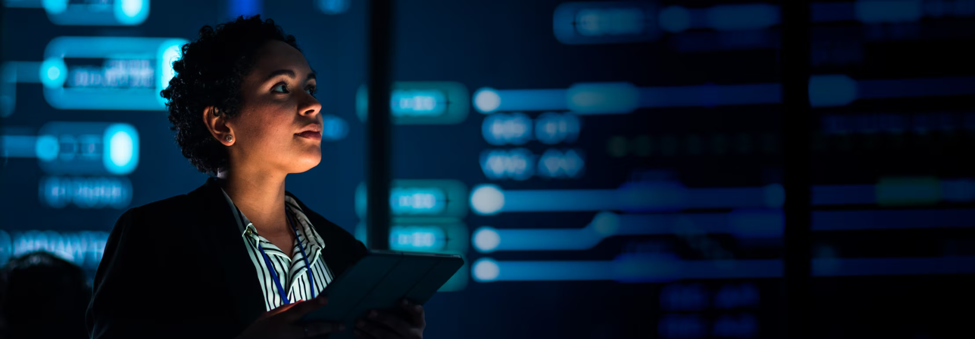 Lady stands in a server room, holding a laptop.