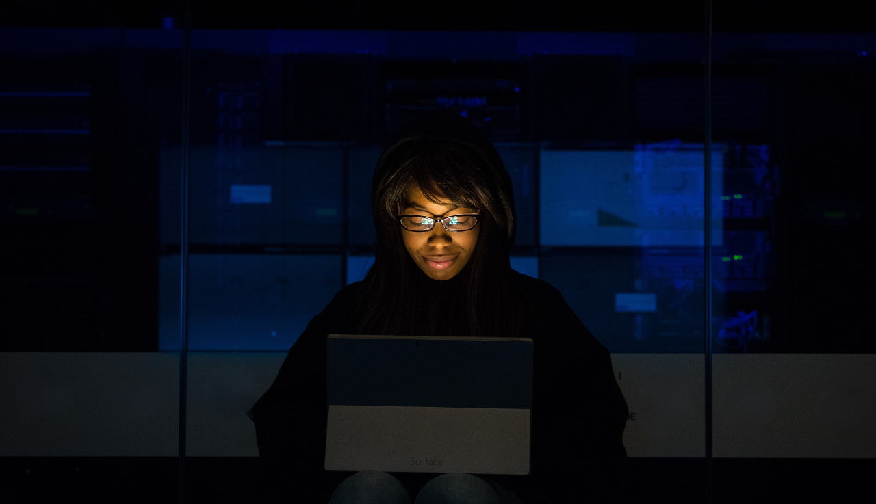 A woman sits with a tablet on her lap in a dark room.