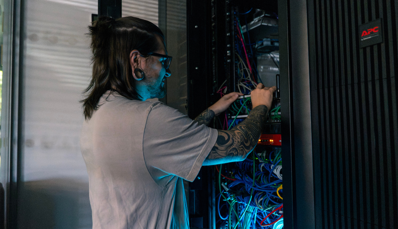 A technical expert stand before an open server cabinet. He is sorting the wiring inside.