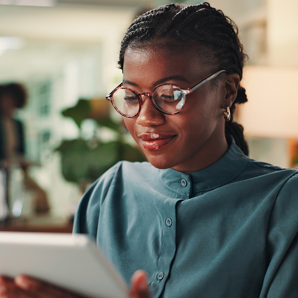Female team member is smiling and looking down at a tablet. The screen is reflected into her glasses.