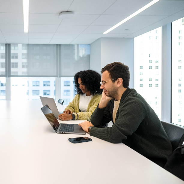 Two staff at a table, each working on their own laptop.