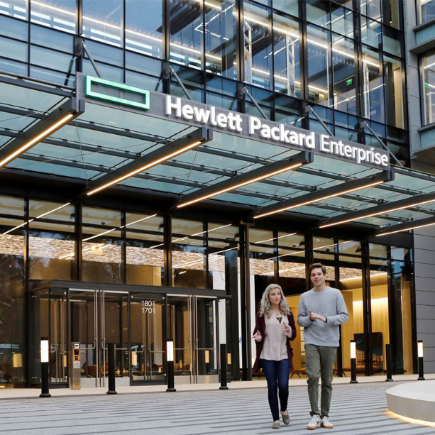 A man and women are walking across the street in from of an office building.