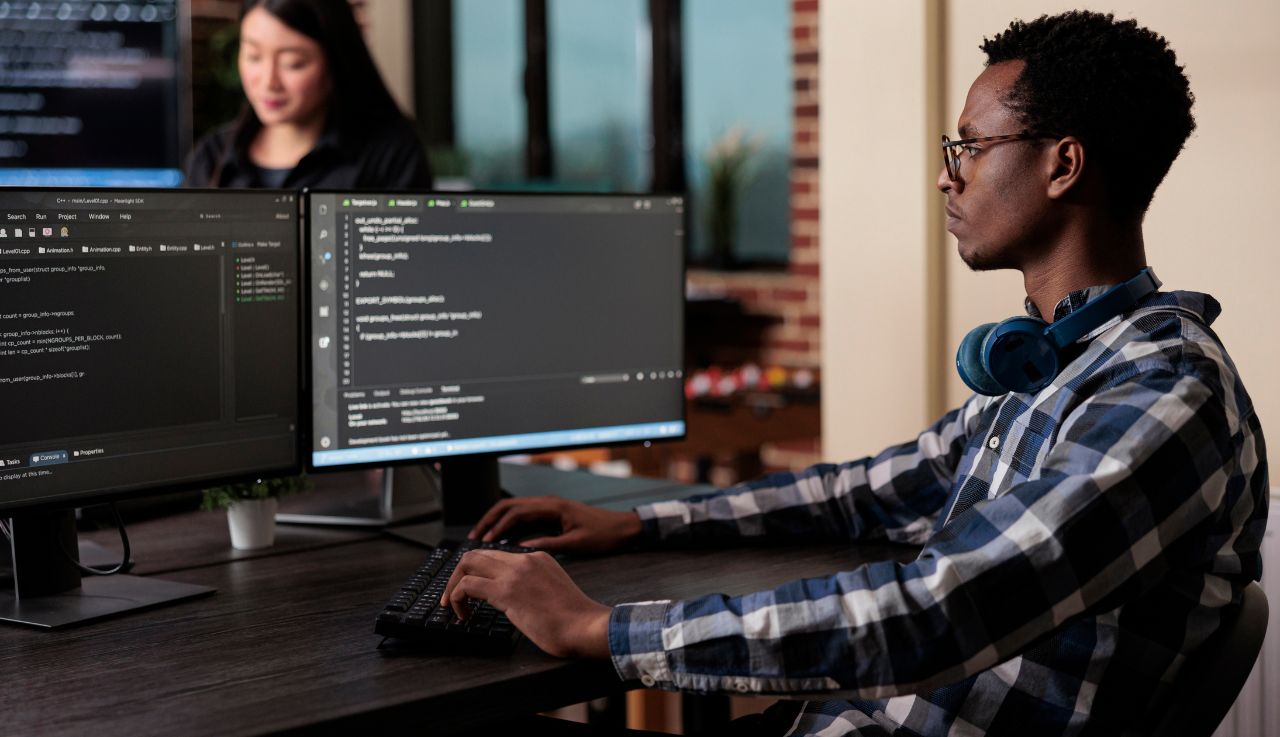 A man sits at his desk, he has headphones around his neck and he's typing.