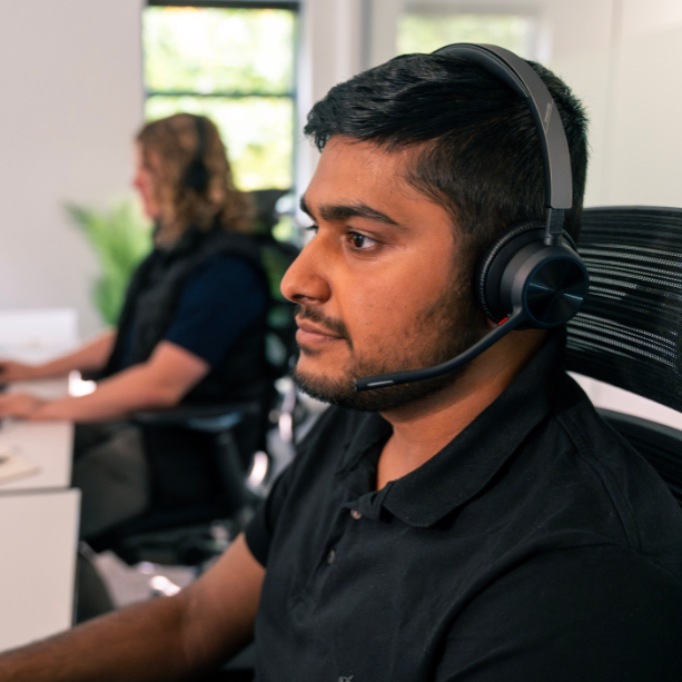 Two male team members are wearing headsets and working at a desk.