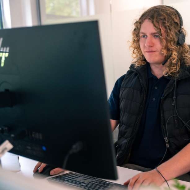 Staff member working at a desk. He's looking at a monitor and wearing a headset.