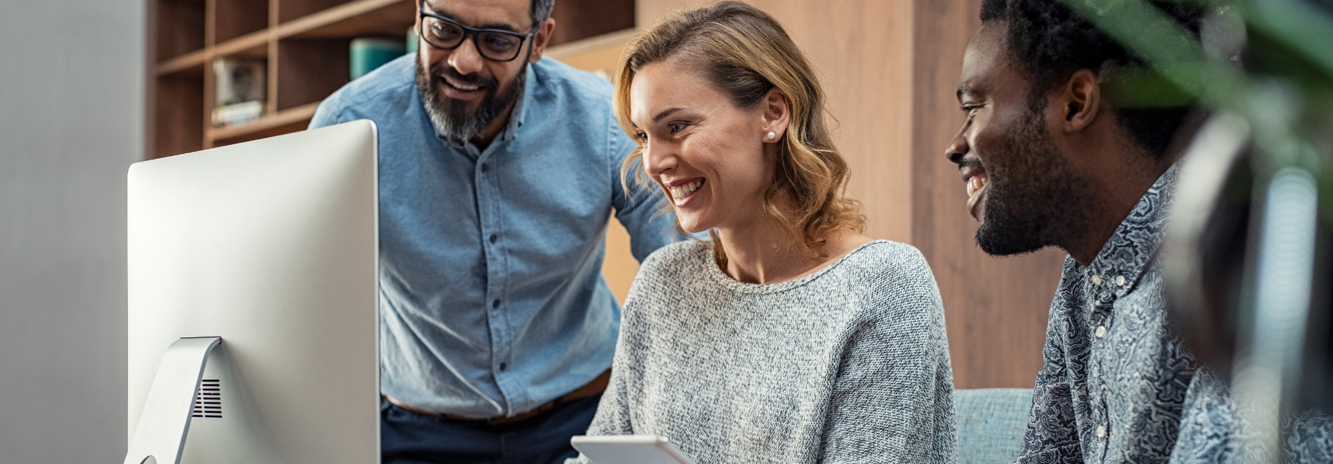 Three staff work around a monitor, two sat, one standing.