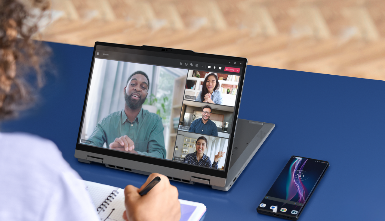 Close up of a table hosting a video call, there are four people on screen and a phone sits beside the tablet.