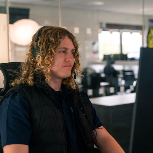 Team member smiling with a headset on facing his desktop.