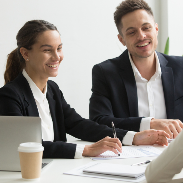 Two staff are conducting an interview, they wear black suits and are smiling.