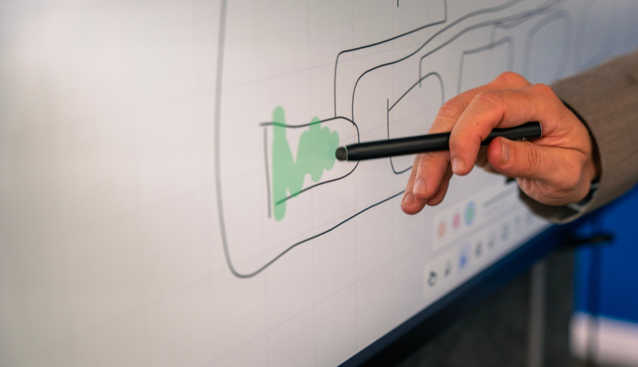 A close up of a smartboard with information on it. Someone is using a stylus to interact with the screen.