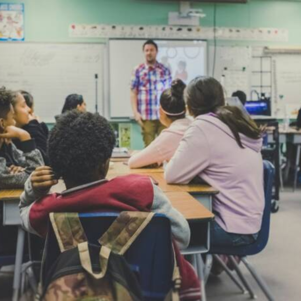Image of a classroom from the back with students facing away from the camera and the teacher at the front