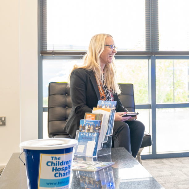 A woman sat in a side profile position with Millgate flyers and The Children's Hospital Charity bucket in the foreground