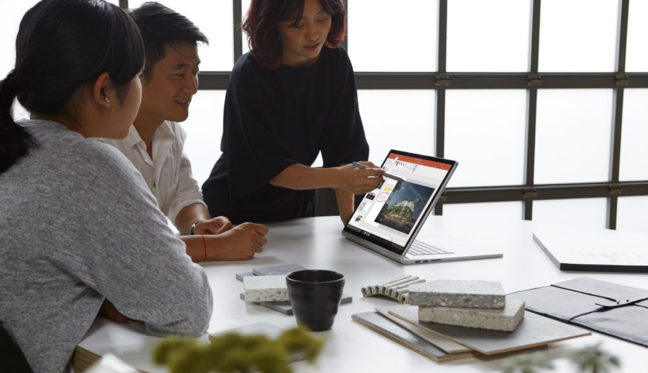 Three people at an office. Two sat looking at the tablet the third lady, stood, is using a stylus to work on.