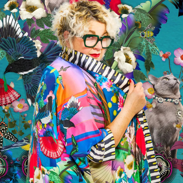 A lady dressed colourfully stand before a graphic background.